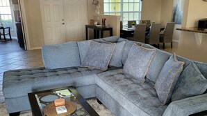 A living room with a sectional sofa, a glass coffee table, and a dining area in the background. - Villa Tortuga - Place to relax (Cape Coral)