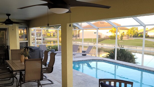 An outdoor patio area with a pool, lounge chairs, a ceiling fan, and a fire feature. - Villa Tortuga - Place to relax (Cape Coral)