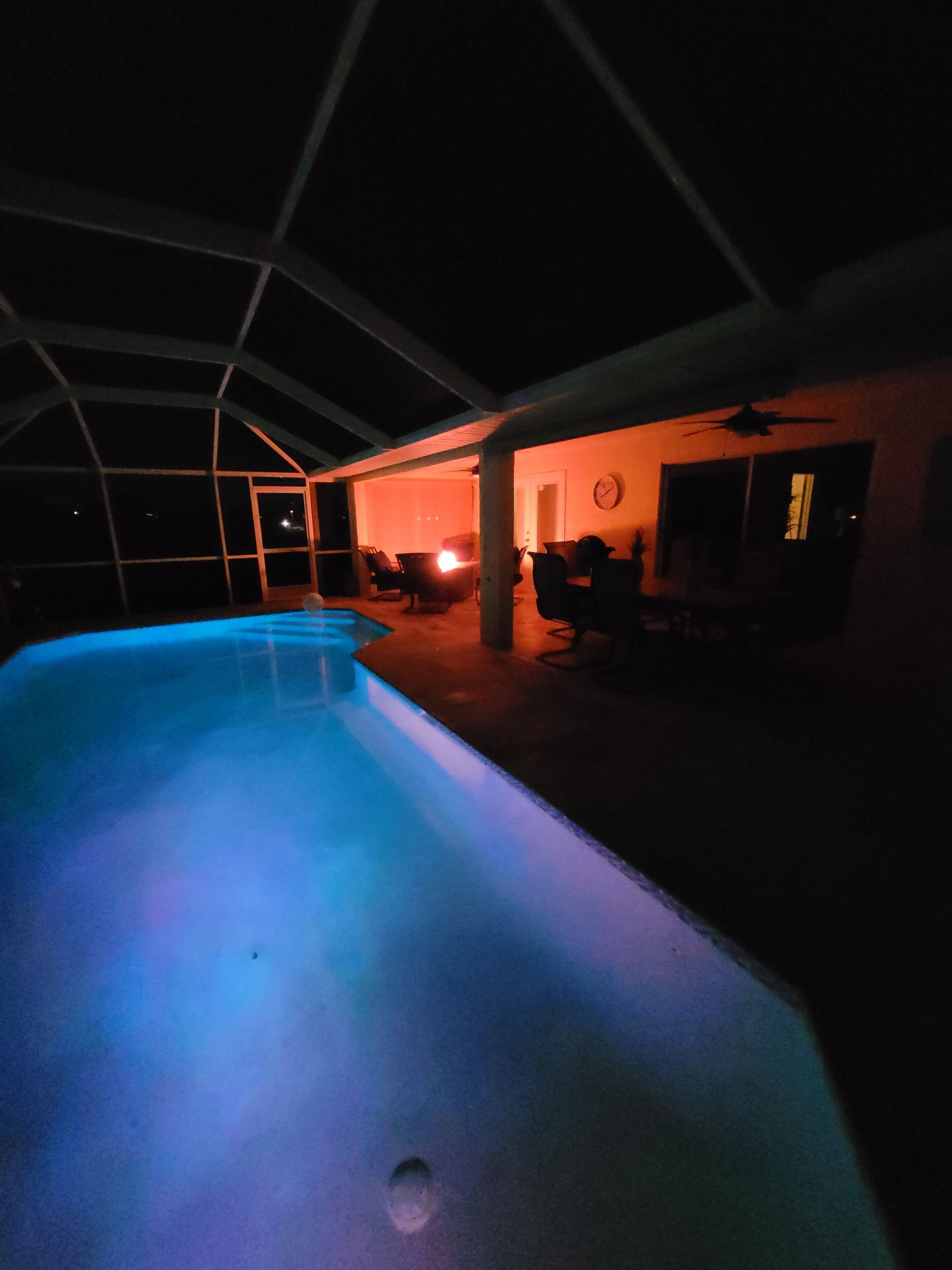 Une piscine à bords incurvés, entourée d’un espace abrité comprenant des chaises et des tables.