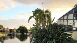 A balcony with two lounge chairs, a water body, and a view of a building across the water. - Villa Tortuga - Place to relax (Cape Coral)