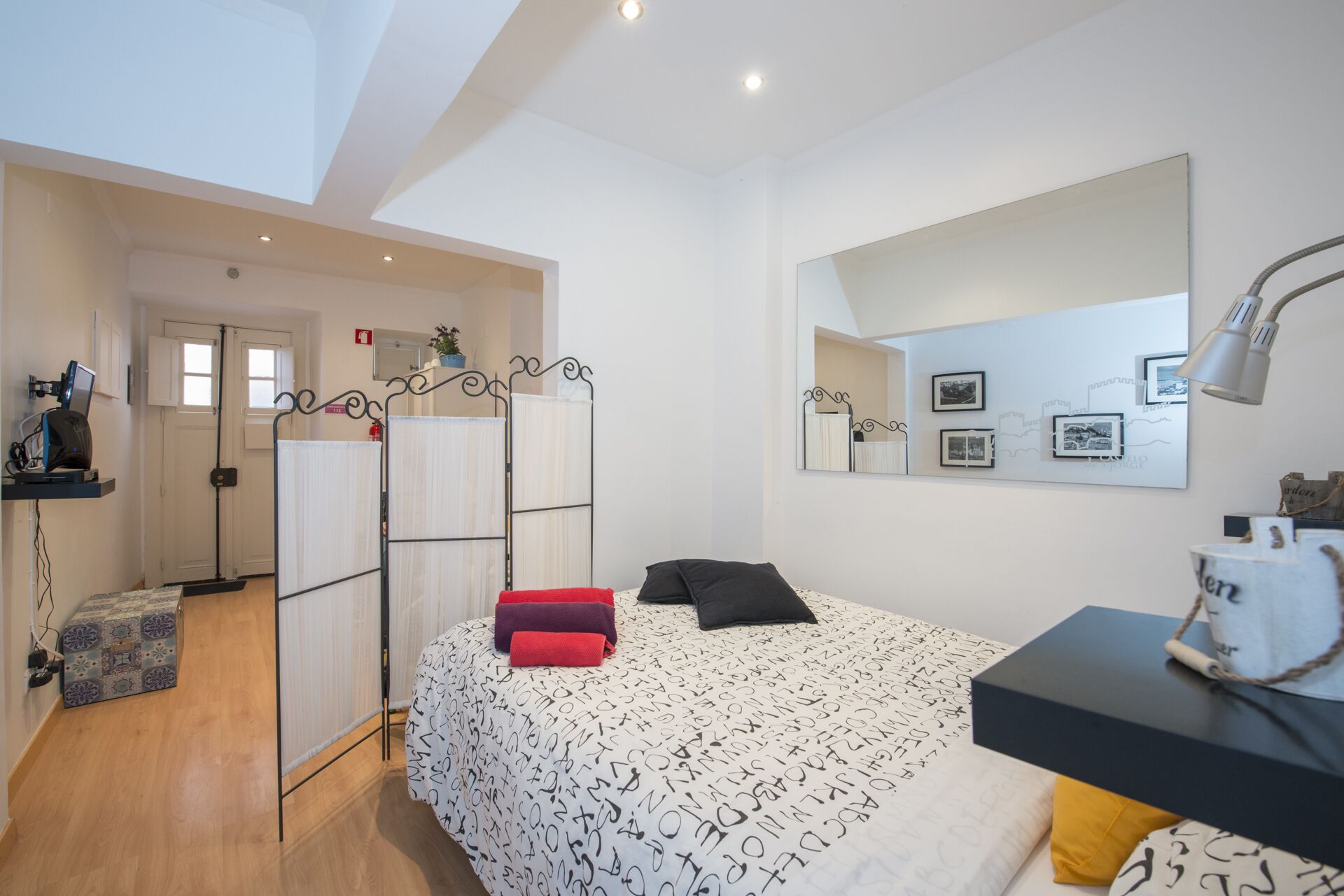 Un dormitorio con cama, escritorio, espejo y una pared con cuadros.