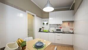 Cocina compacta con armarios blancos, un microondas, un tostador y un lavamanos. Hay una mesa de comedor con un cesto de plátanos y una planta en maceta.