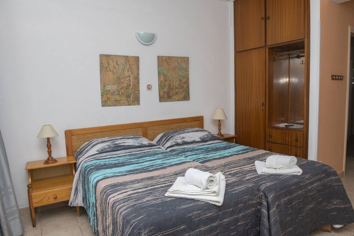 A bedroom with a wooden bed, two bedside tables with lamps, a wardrobe, and two wall-mounted paintings.