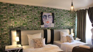 A hotel room with two beds, a brick-patterned wall, a painting above the beds, and a nightstand with a lamp. - Stoneybrooke farm (Tierpoort)