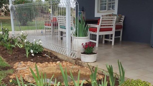 A garden with a variety of plants, a white fence, and a seating area with a table and chairs. - Stoneybrooke farm (Tierpoort)