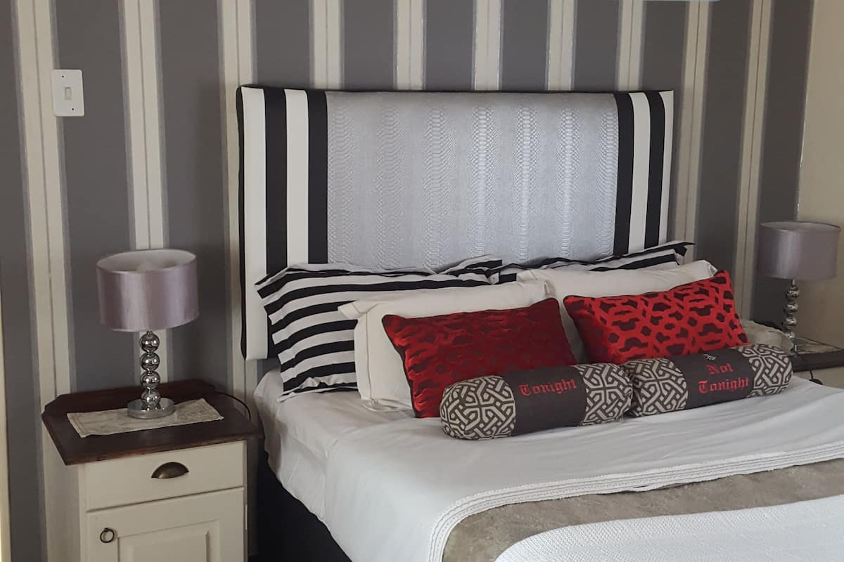 Un lit bien fait, avec une literie à rayures, un coussin à motifs et une lampe de chevet posée sur une table de nuit.