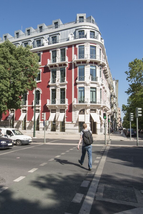 Una esquina de calle con un edificio rojo de arquitectura ornamentada, un paso de peatones y un semáforo.