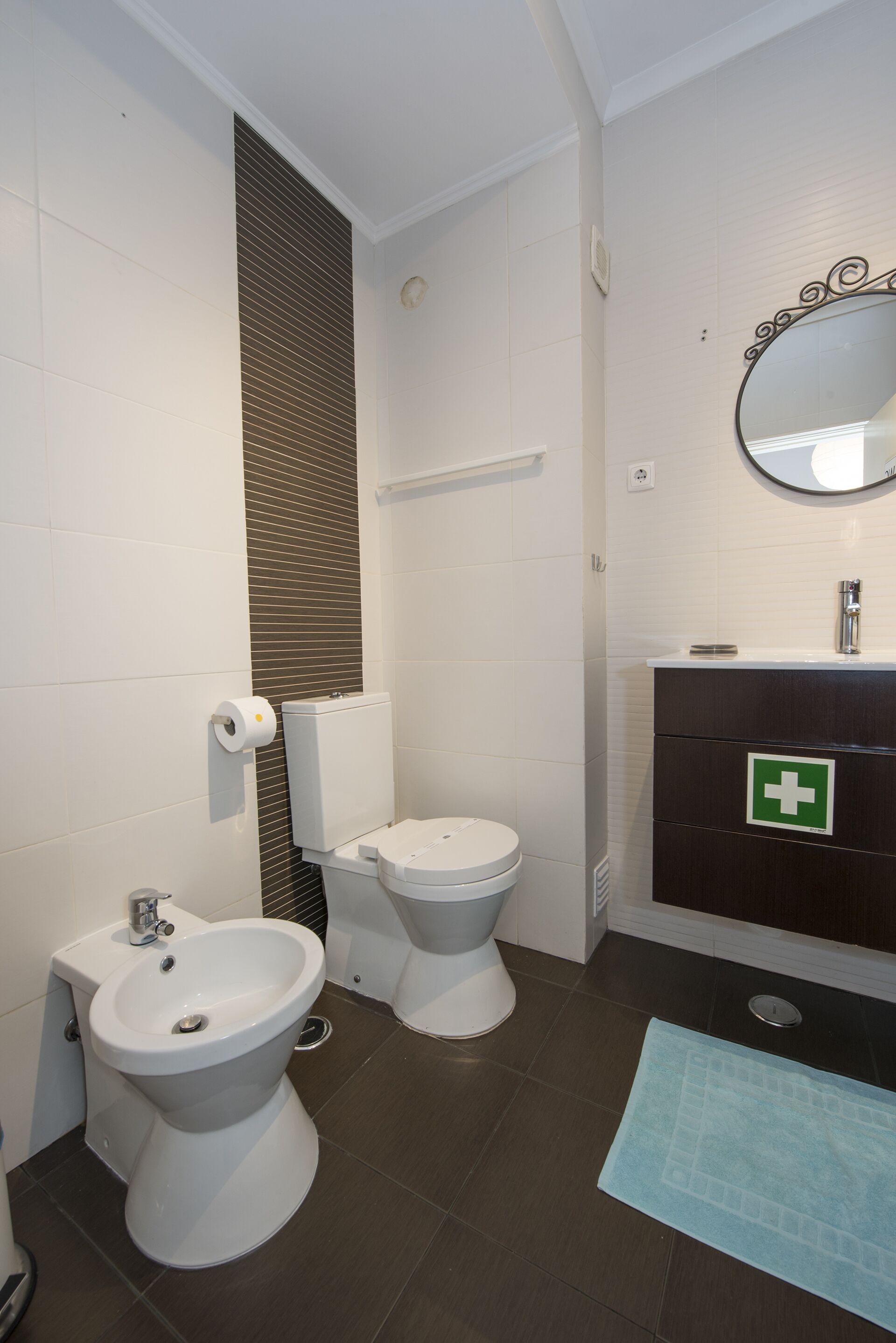 A bathroom with a bidet, toilet, sink, and mirror.