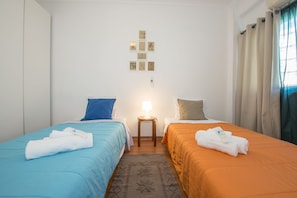 Una habitación de hotel con dos camas, una mesita con lámpara y una pared decorada con cuadros.