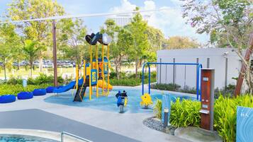 Un parque infantil con toboganes y estructuras de escalada, rodeado de follaje y una zona de piscina.