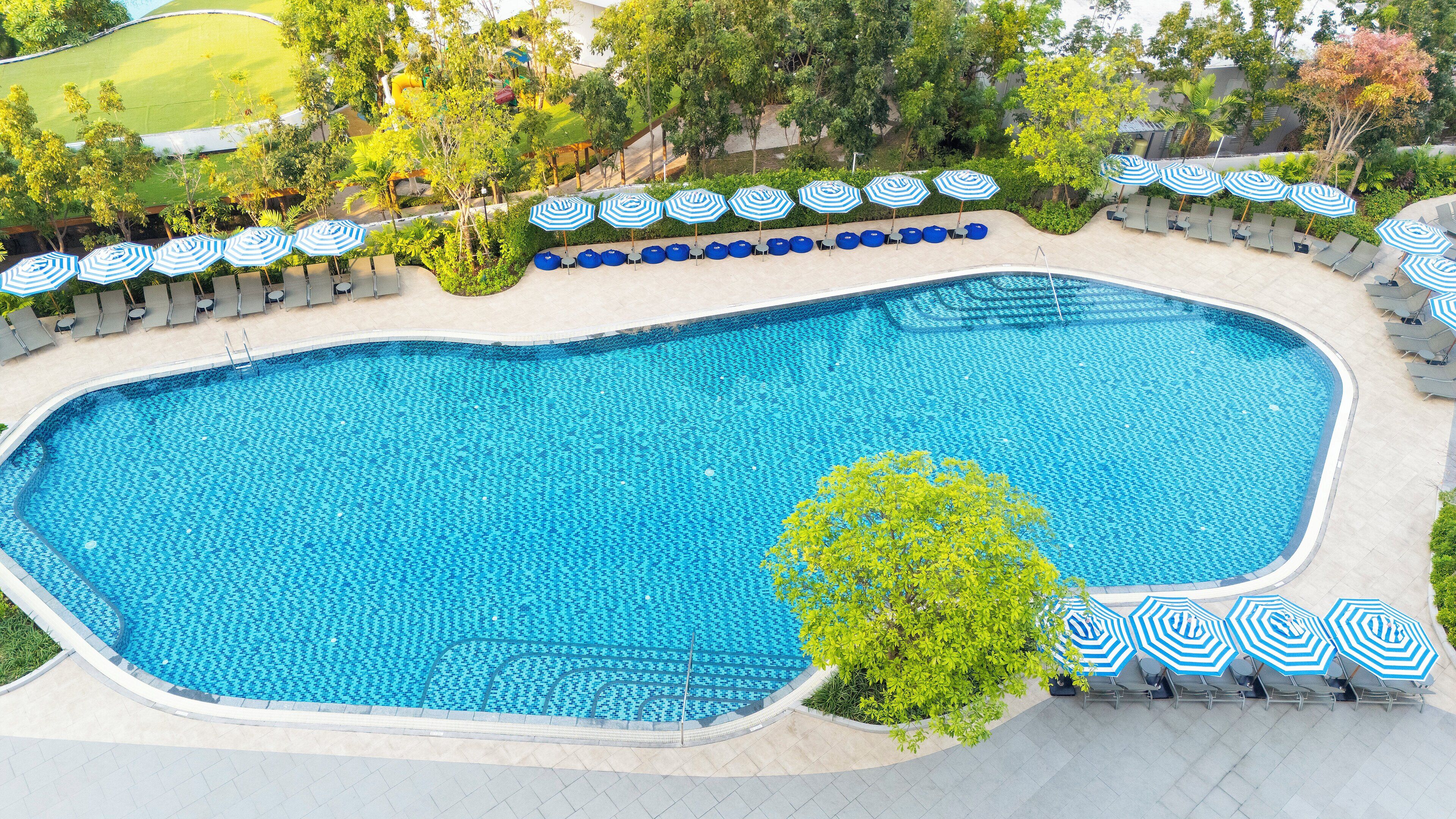A large outdoor swimming pool with blue tiles, surrounded by lounge chairs and umbrellas.