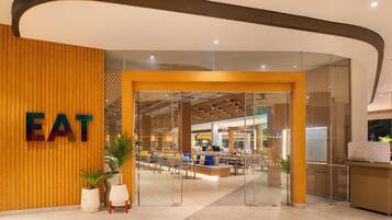 A modern eatery with a wooden wall and a glass entrance. Inside, there are tables and chairs arranged for dining.