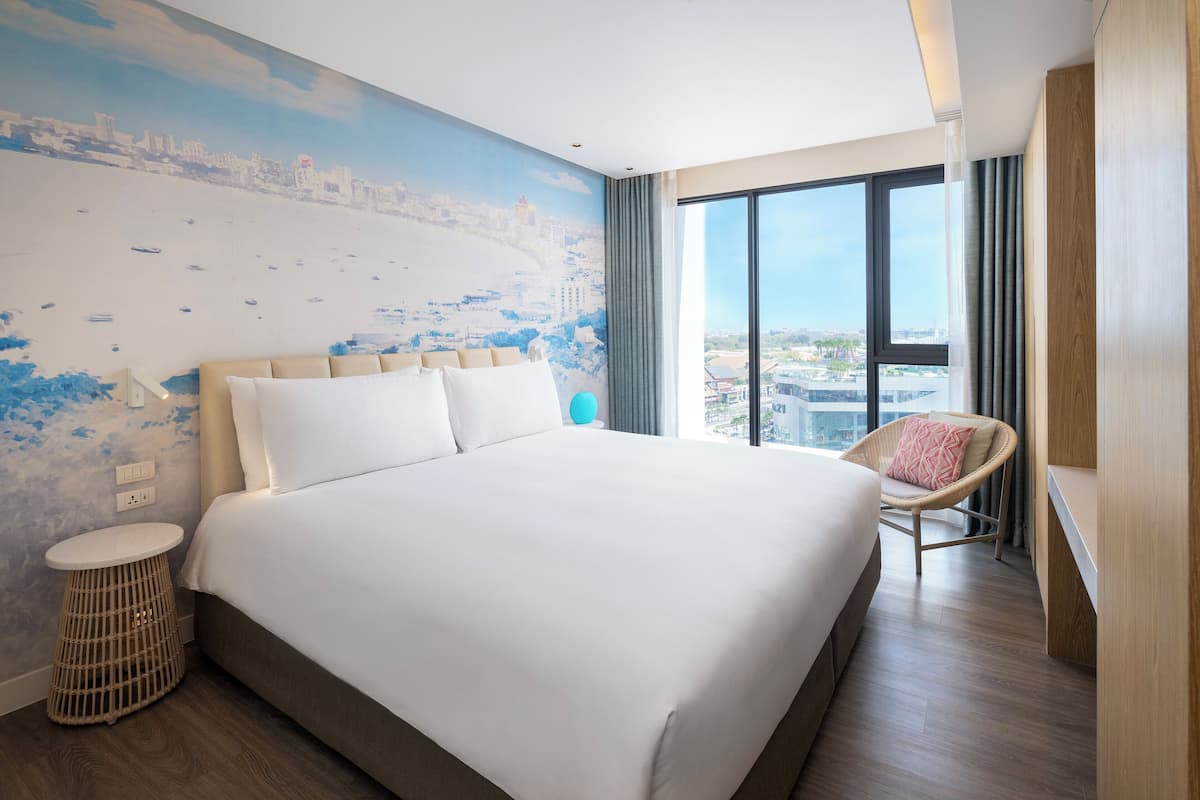 Habitación de hotel moderna con una cama grande, un mural de paisaje urbano en la pared, vistas desde la ventana y una silla de mimbre.