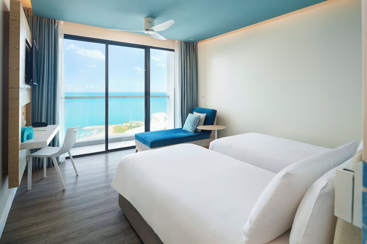 Habitación de hotel con un ventanal grande, una cama, un escritorio con silla y una mesita.