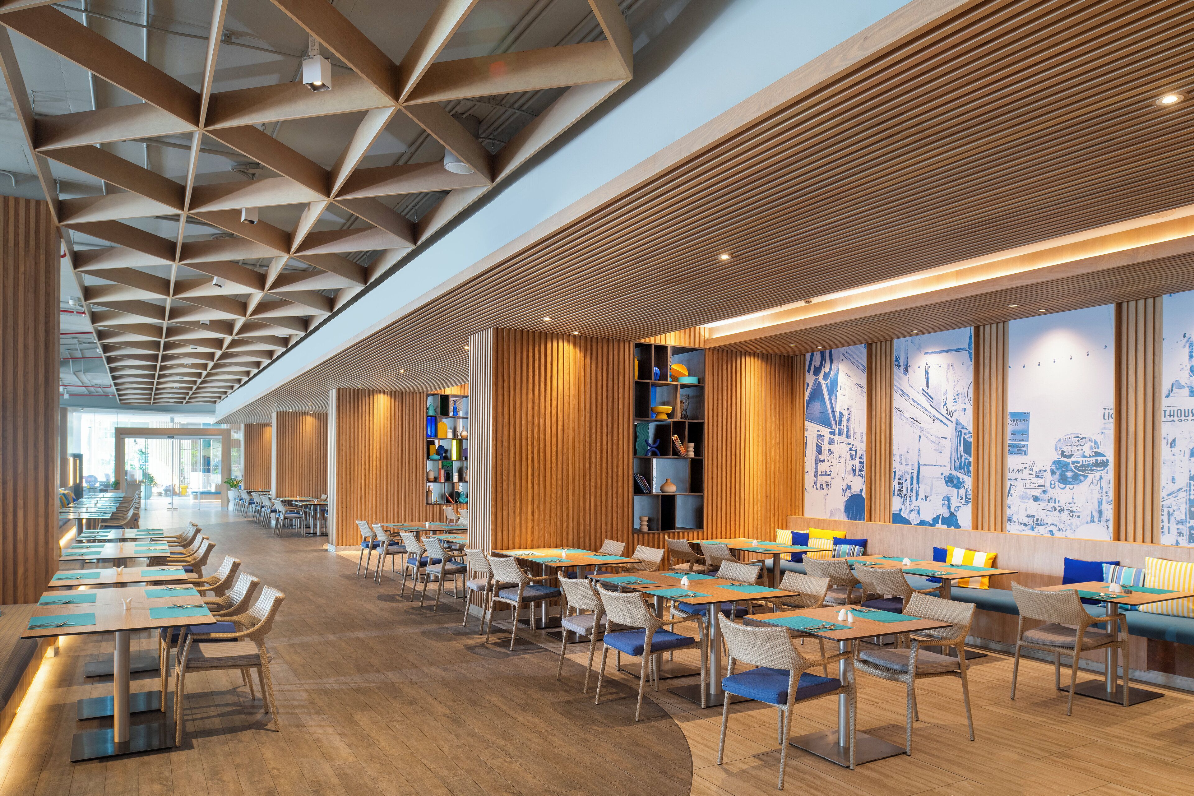 A spacious restaurant with long tables and chairs, wooden paneling on the walls, and large windows.