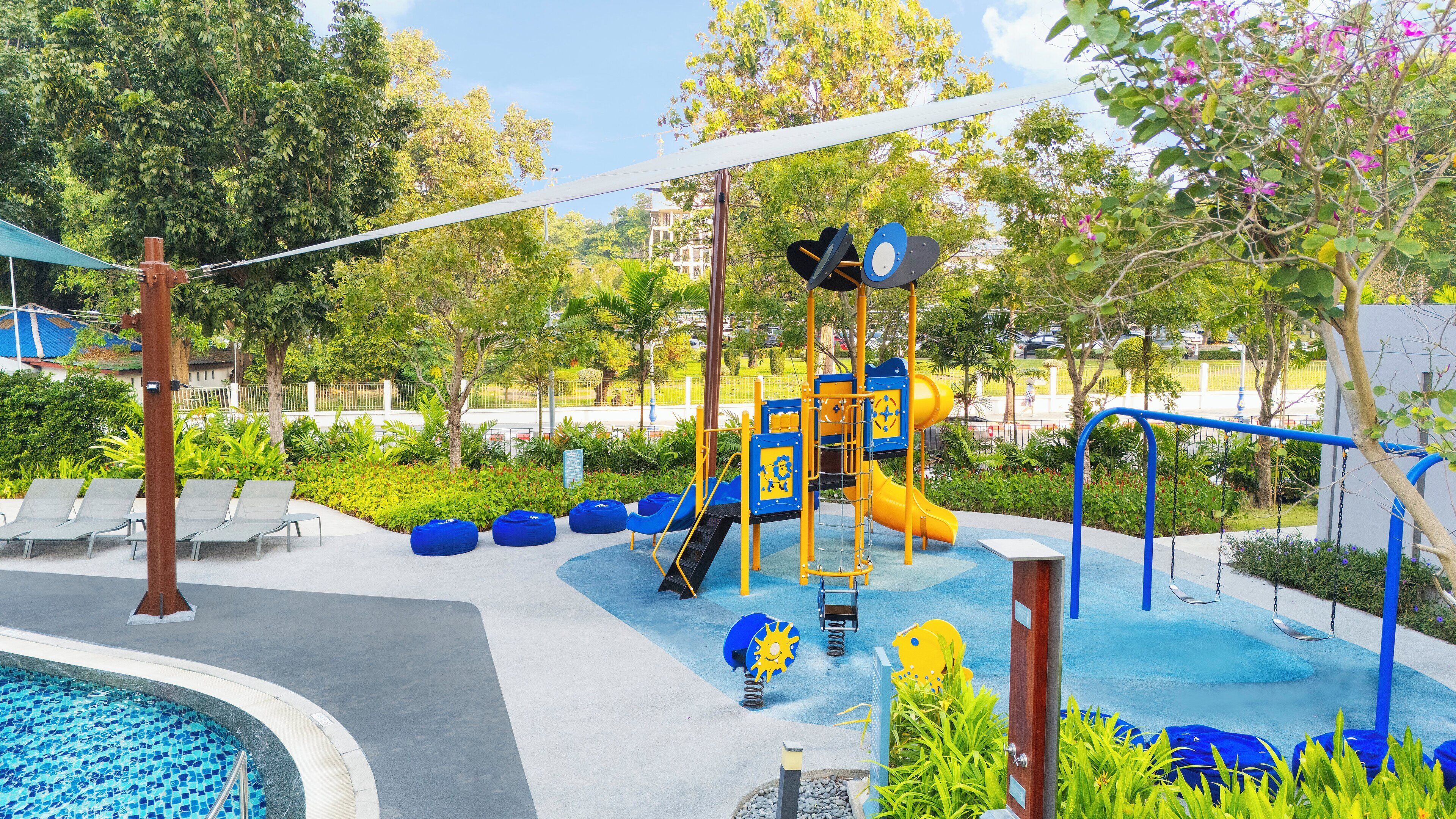 A playground with slides and climbing structures, surrounded by seating areas and a pool.