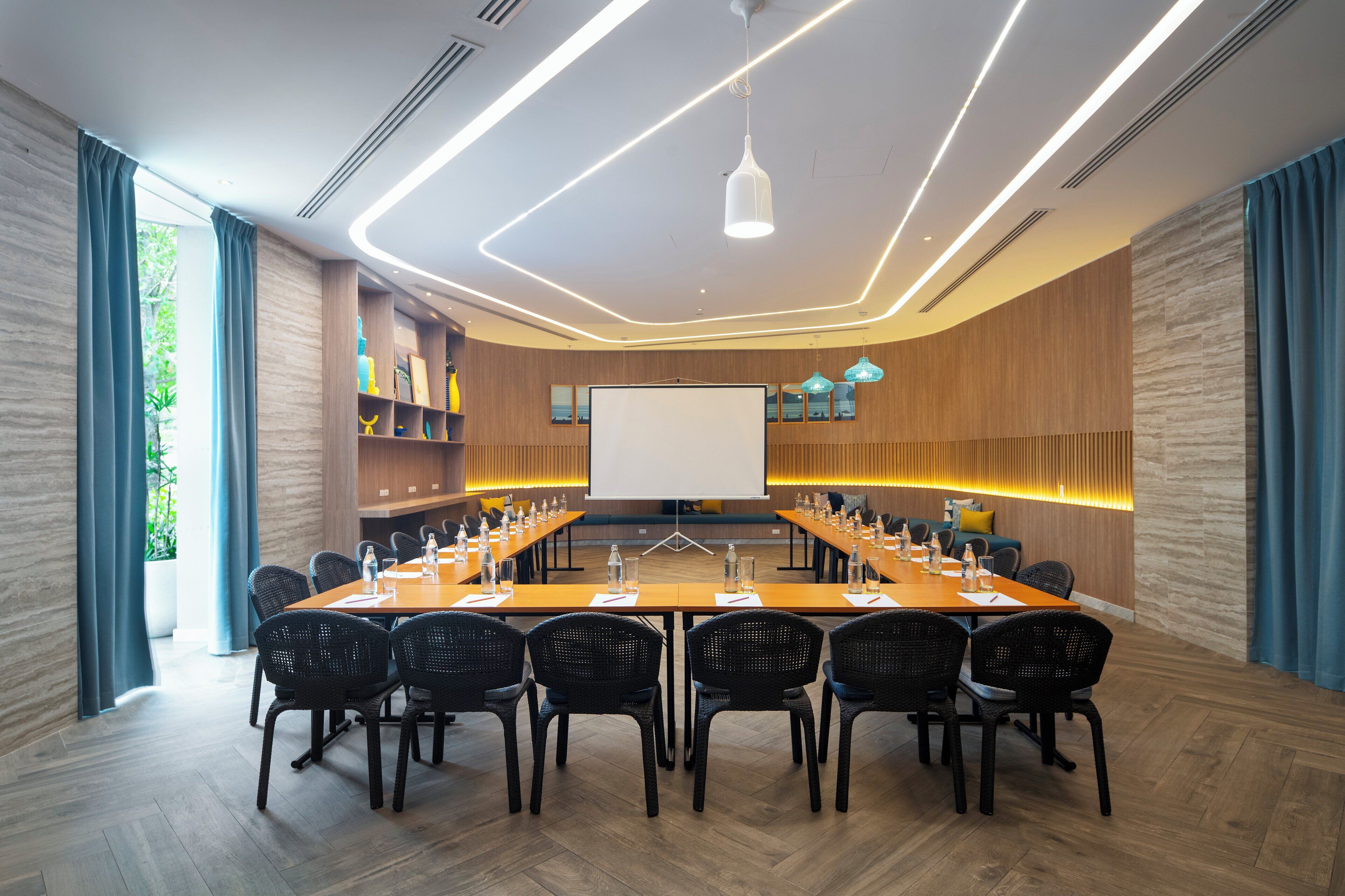 A conference room with a long table, black chairs, a whiteboard, and a projector screen.