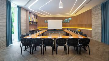 A conference room with a long table, black chairs, a whiteboard, and a projector screen.