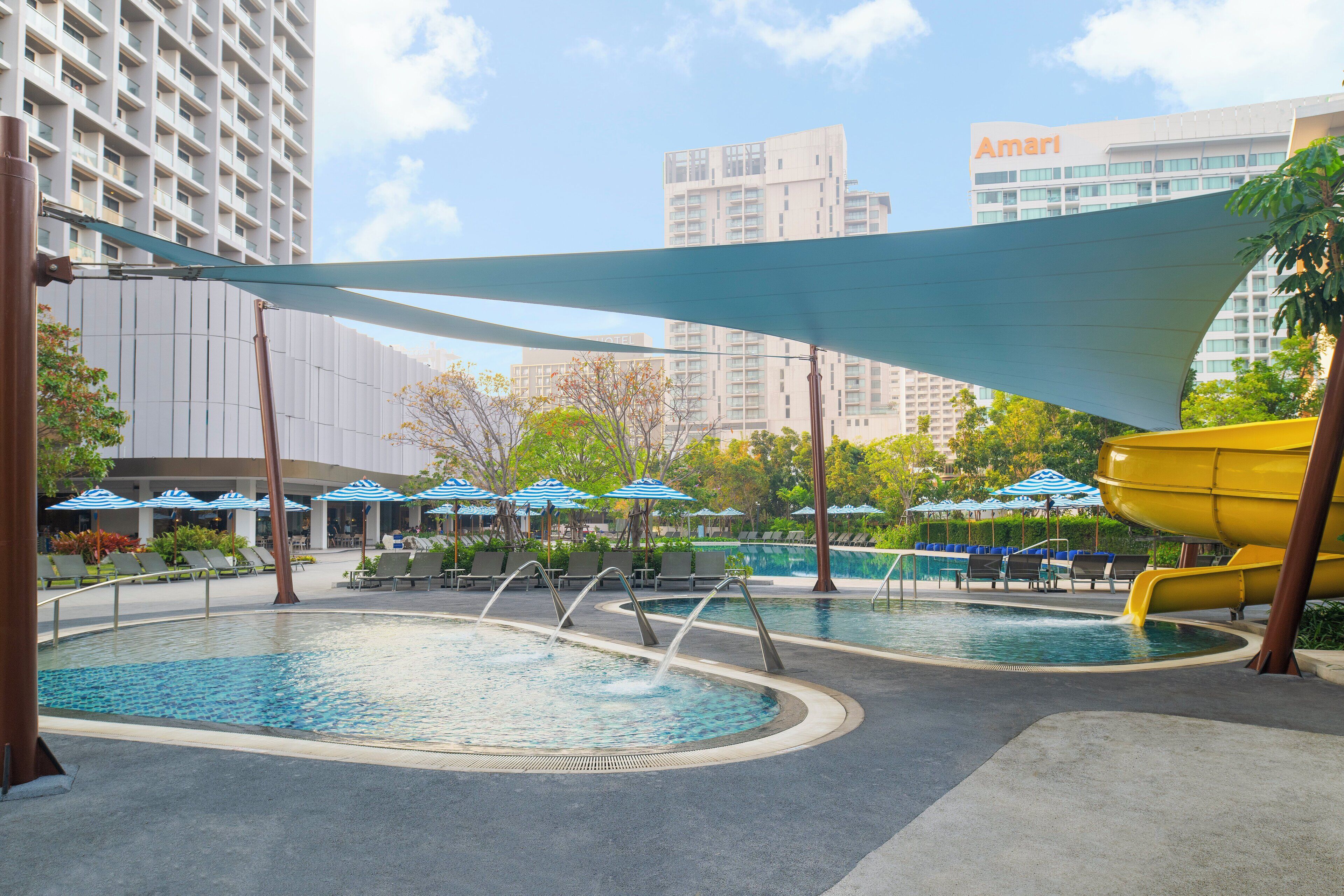 A pool area with multiple water features, lounge chairs, and umbrellas.