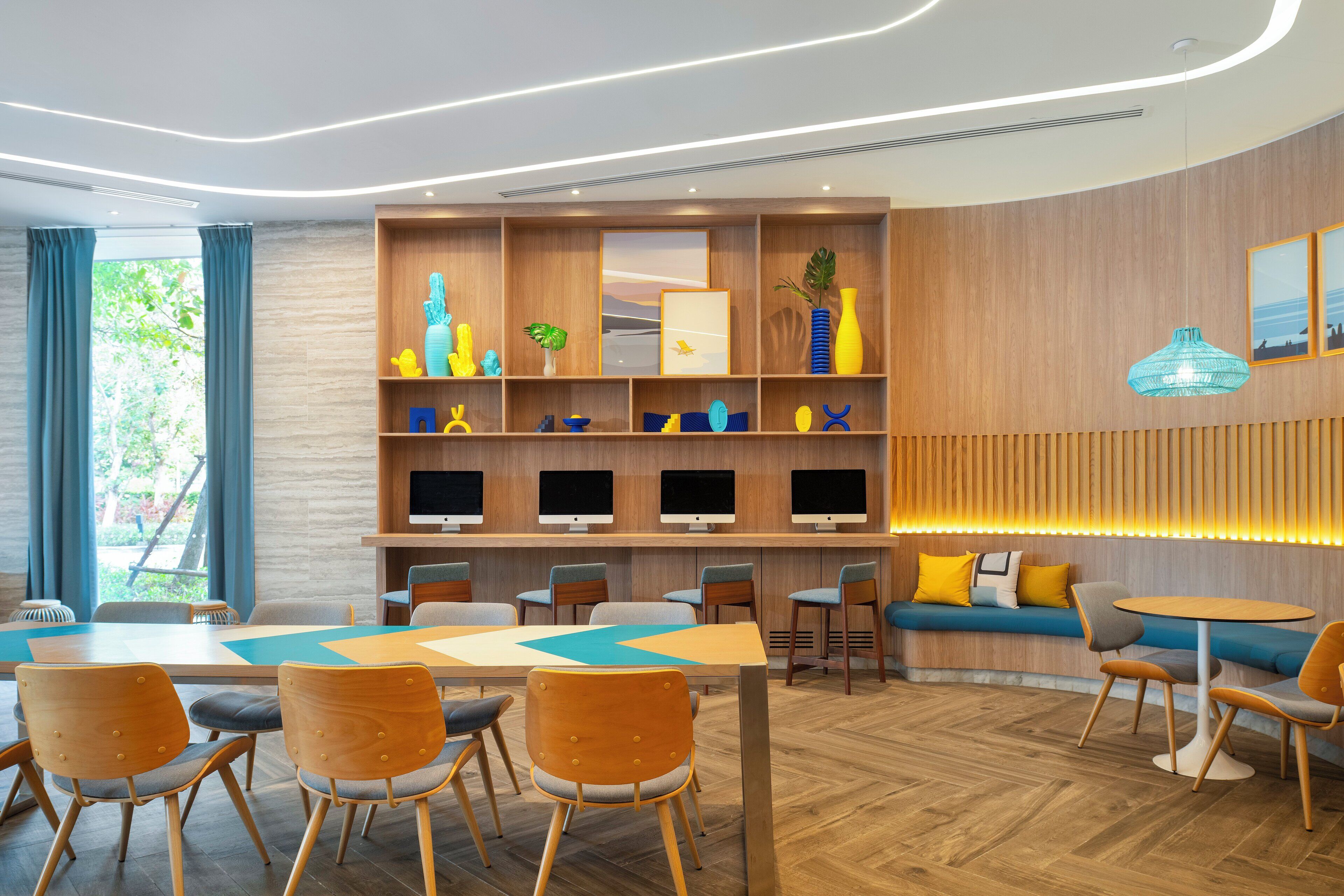 A modern hotel lobby with a wooden reception desk, seating area, and a wall-mounted TV display.