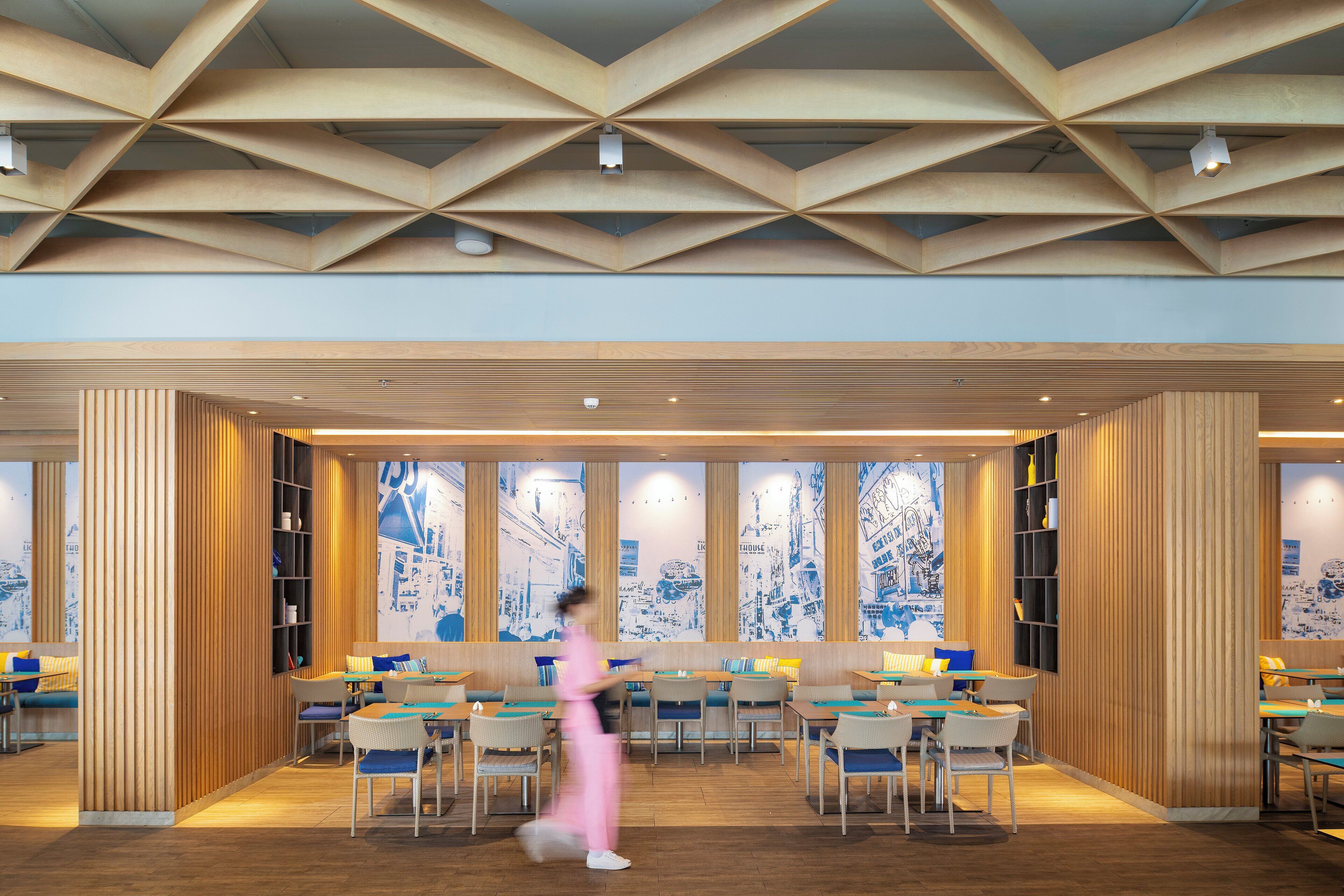 A modern interior with a geometric ceiling design, wooden paneling, and a cityscape mural on the walls.