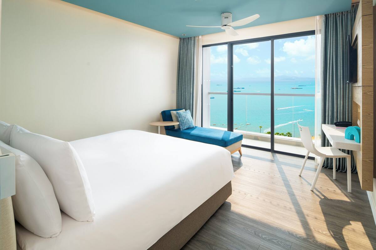 Una habitación de hotel moderna con una cama grande, un escritorio y vistas al mar.