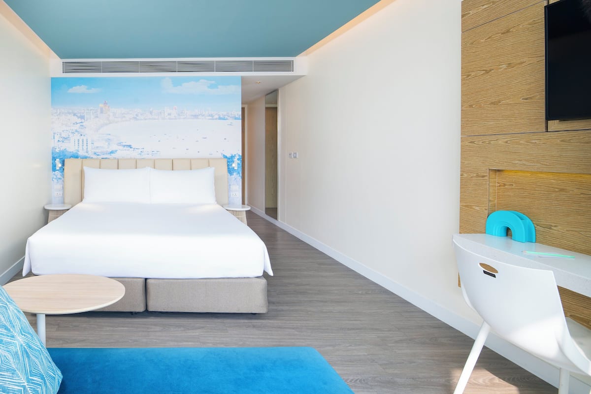 Una habitación de hotel moderna con una cama grande, un escritorio pequeño y un televisor en la pared.