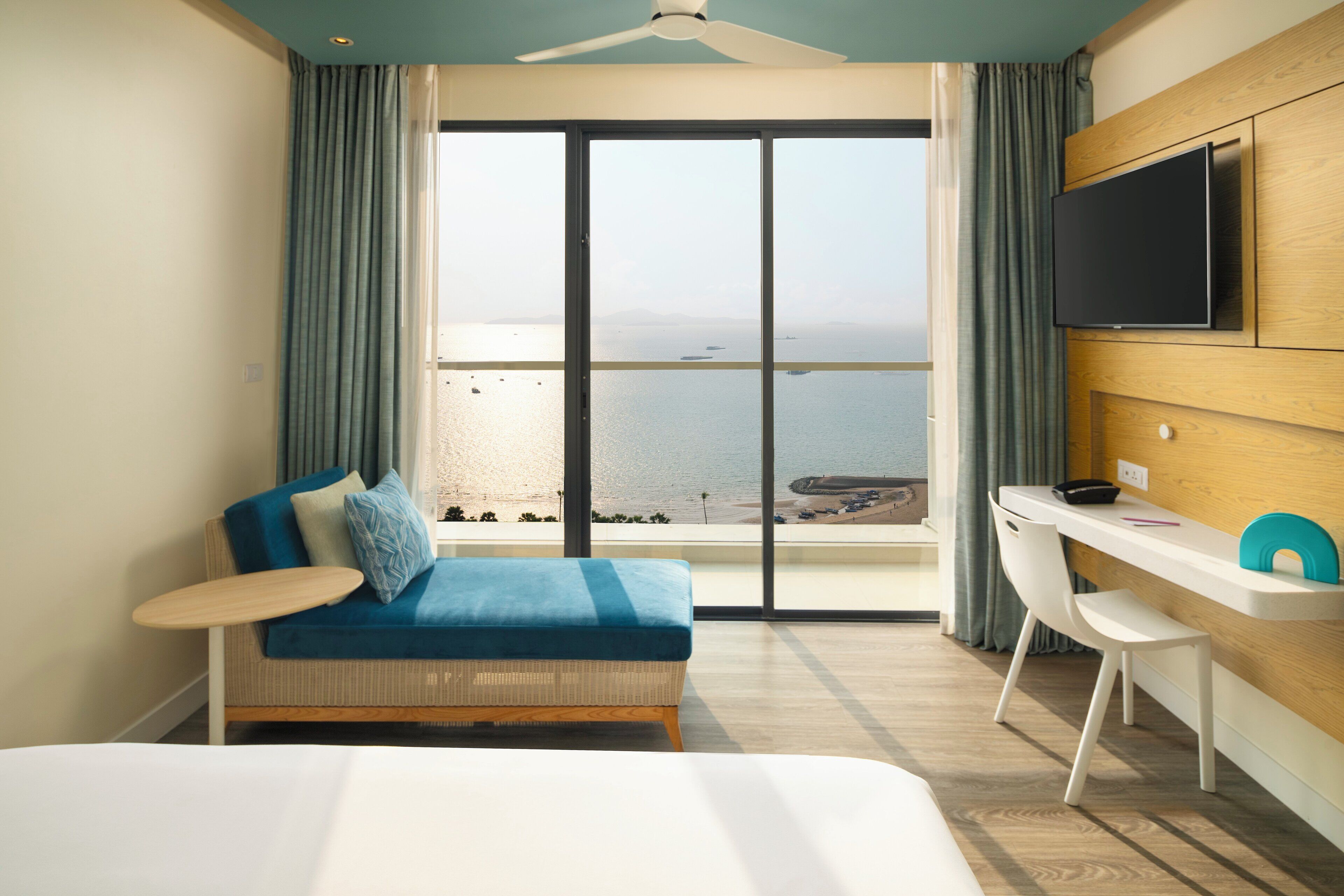 Una habitación de hotel con un ventanal grande, una cama, un escritorio y un televisor.