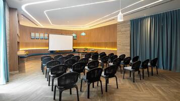 A conference room with rows of chairs, a whiteboard, and a wooden reception desk.