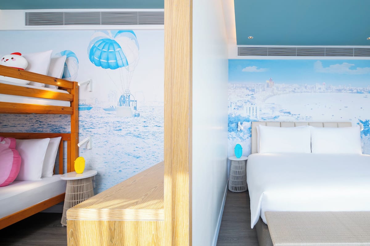 Una habitación con una litera, una cama individual, una mesa de madera y un mural en la pared que representa una escena de playa.