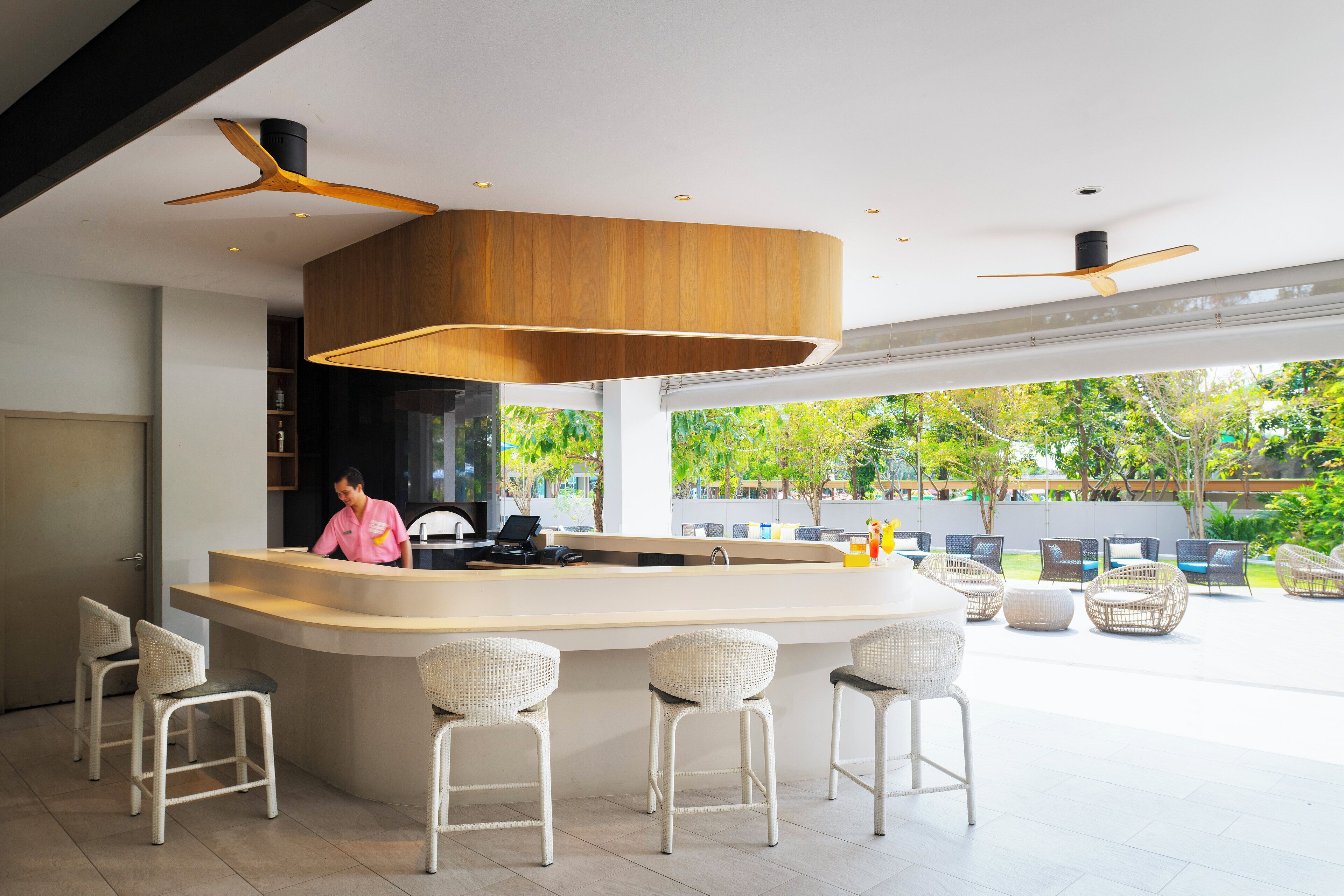 A modern bar area with a wooden ceiling, bar stools, and a view of the outdoor garden.
