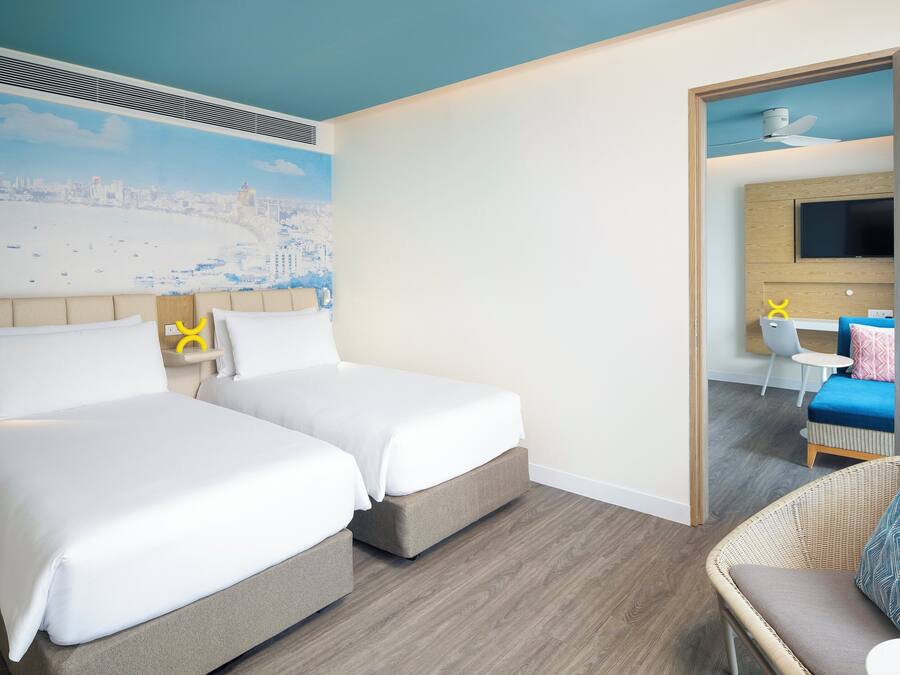 Habitación de hotel con dos camas, un mural de la ciudad, un televisor y una silla de mimbre.