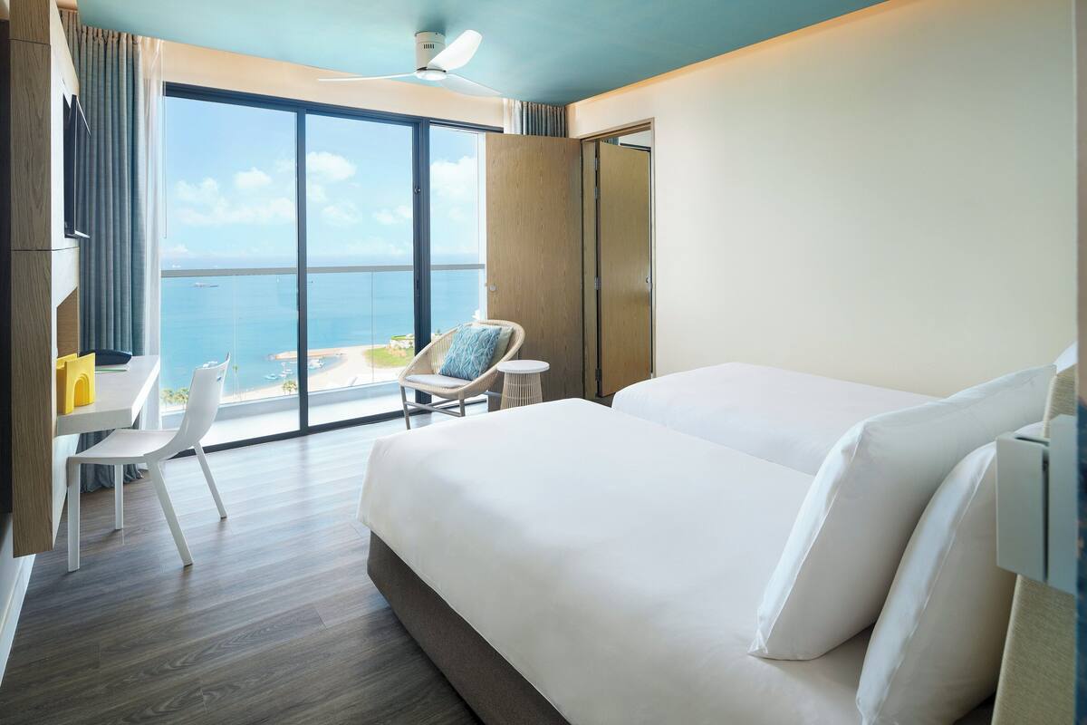 Habitación de hotel con una cama grande, una silla, una mesita y vista al océano.