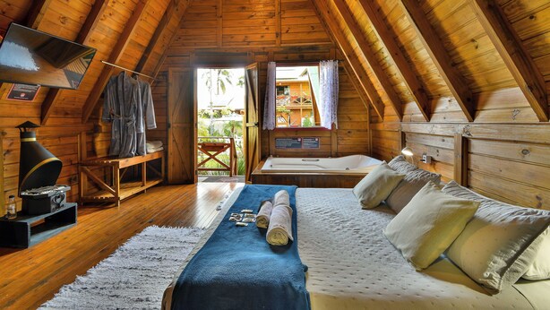 Una habitación acogedora tipo cabaña de madera con una cama, una mesita con una radio y una ventana con cortinas.