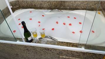 Una bañera con pétalos de rosa flotando en el agua, una botella de champán y dos copas.