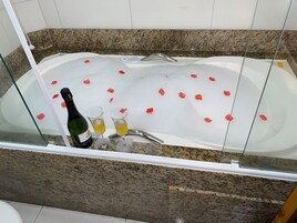 Una bañera con pétalos de rosa flotando en el agua, una botella de champán y dos copas.