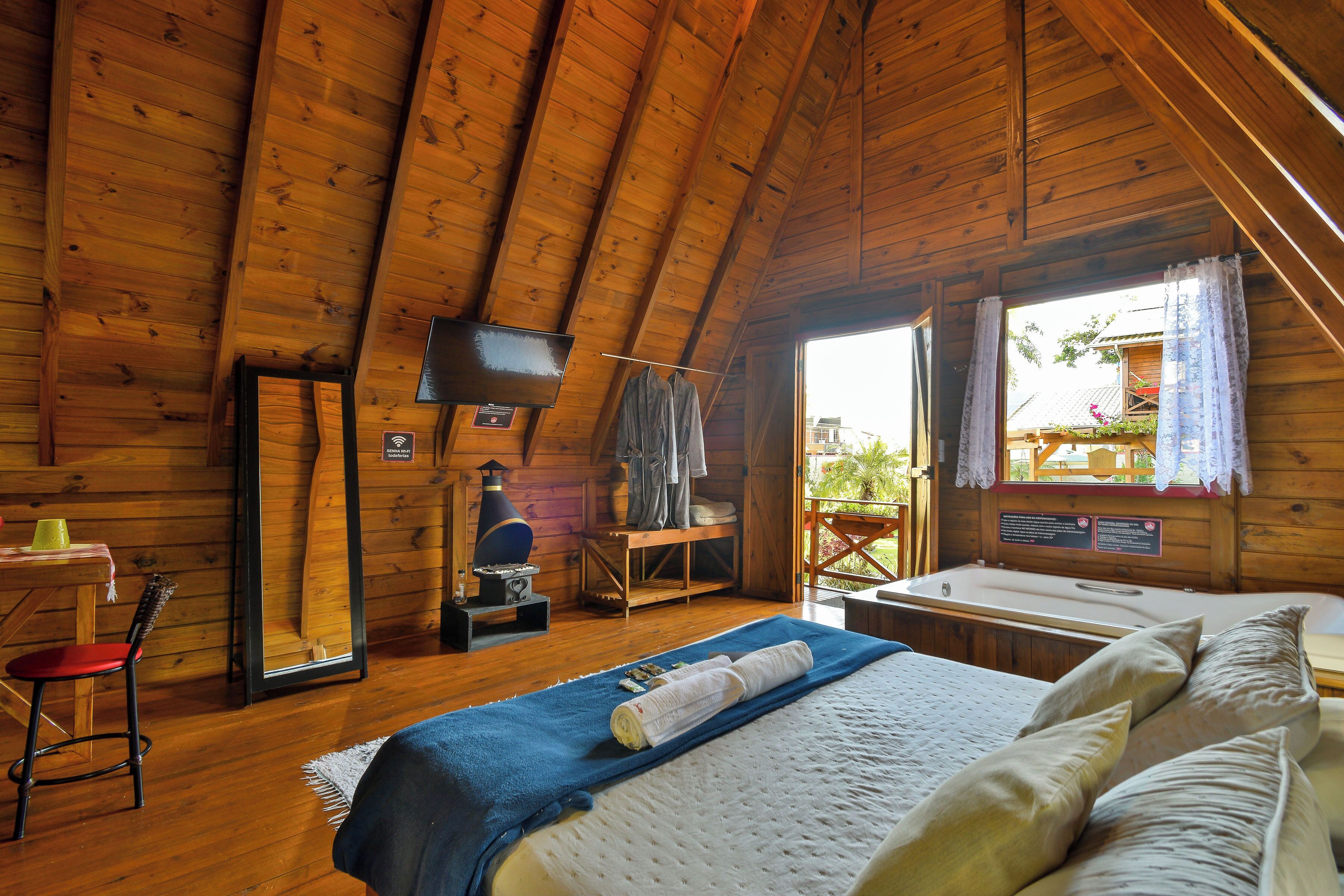 A cozy wooden cabin with a bed, a wooden table, a chair, a TV, and a window with curtains.