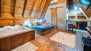 Un dormitorio acogedor en el ático con techo inclinado de madera, una bañera grande y una pequeña kitchenette.