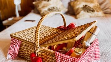 A wicker basket with a red and white checkered cloth, containing a bottle, a jar, and a red ornament, placed on a bed with a white textured cover.