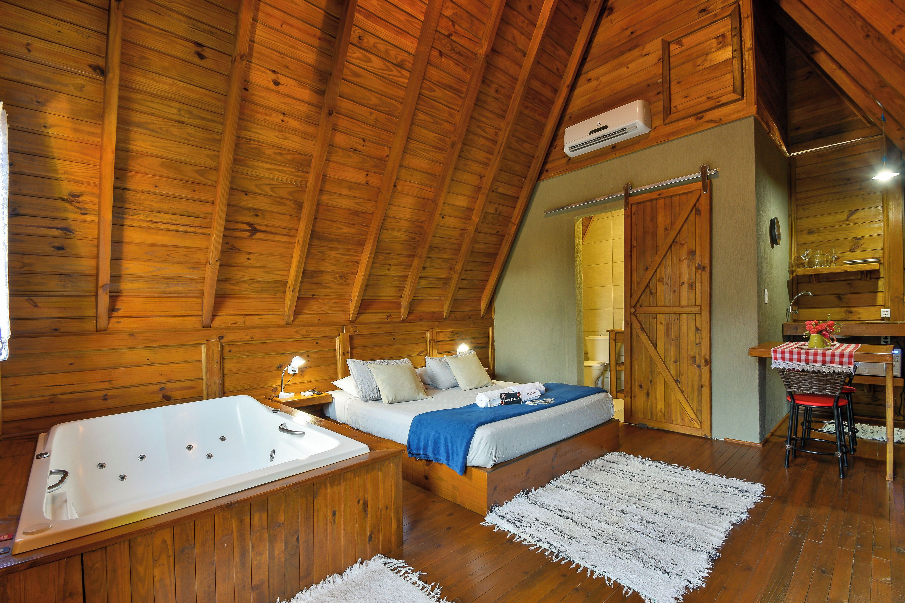 Un dormitorio tipo cabaña de madera con una cama grande, un baño separado con bañera y una zona de comedor con mesa y sillas.