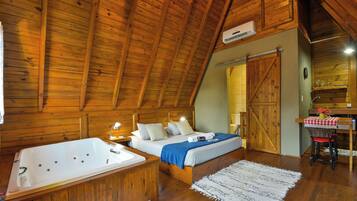Un dormitorio tipo cabaña de madera con una cama grande, un baño separado con bañera y una zona de comedor con mesa y sillas.