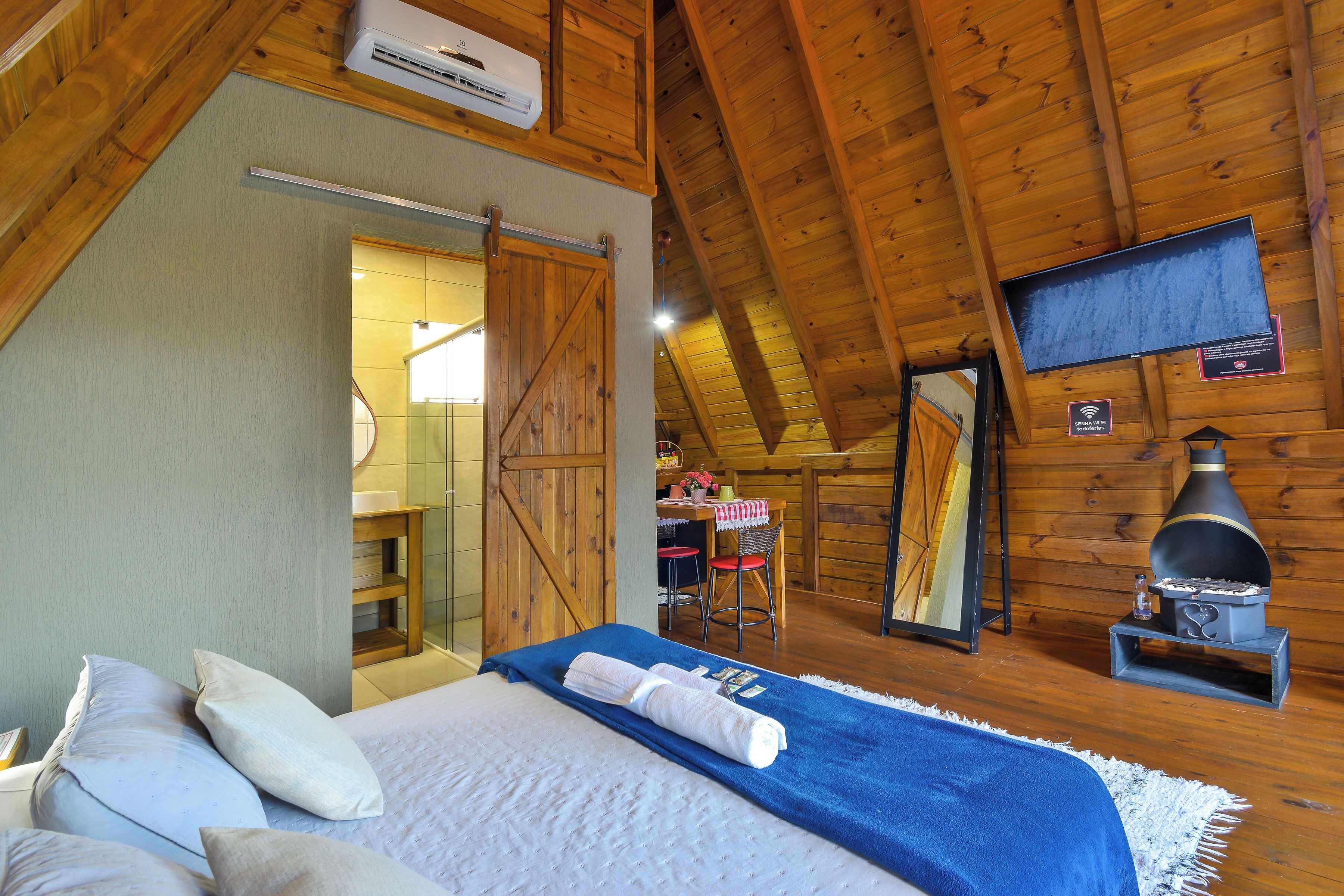 Una habitación acogedora con cama, techo de madera, televisor y chimenea.