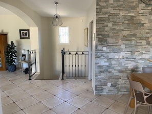 Um quarto espaçoso com piso de azulejos, parede de destaque em pedra, área de jantar com mesa e cadeiras, e um portão de metal decorativo.