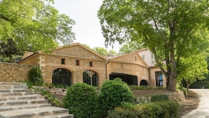 A stone building with a staircase leading to a door, surrounded by greenery and trees. - Chateau Mentone (Saint-Antonin-du-Var)