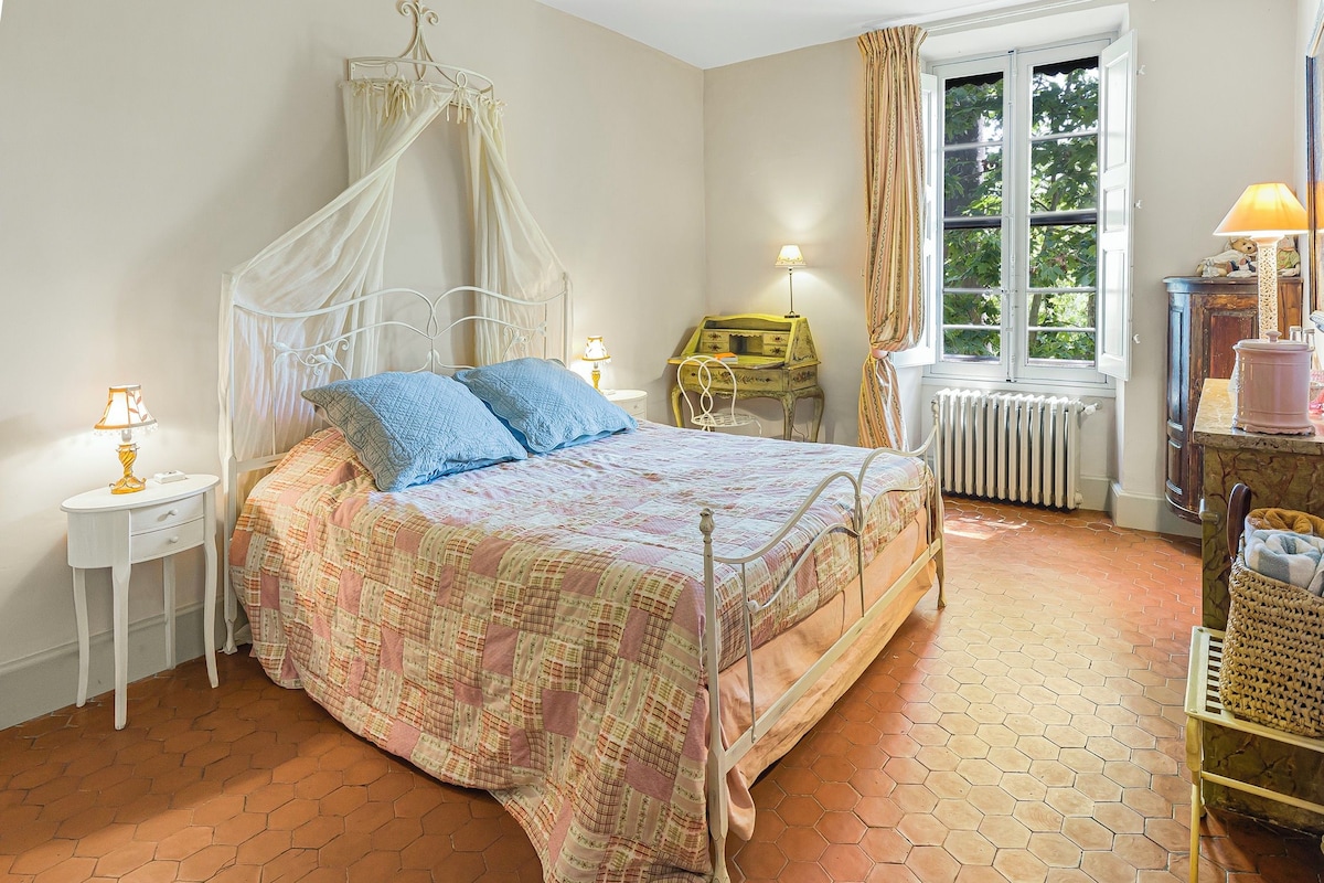 Un dormitorio con cama con dosel, mesita de noche, cómoda y ventana con cortinas.