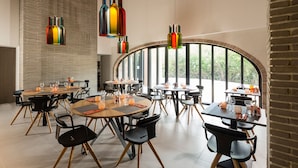 A modern dining area with round tables and black chairs, large windows, and hanging colorful bottles. - Chateau Mentone (Saint-Antonin-du-Var)