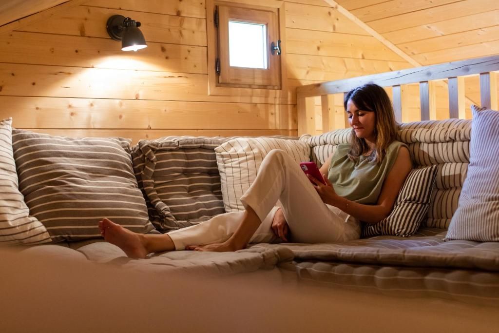 Een persoon zit op een bed in een kamer met houten wanden en een schuine plafond.