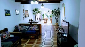 A living room with a sofa, a coffee table, and a TV. There are potted plants and a dining area in the background. - Deck Hostel Congonhas (São Paulo)