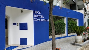 A building with a blue and white facade, labeled "DECK HOSTEL CONGONHAS," featuring a door, windows, and potted plants. - Deck Hostel Congonhas (São Paulo)