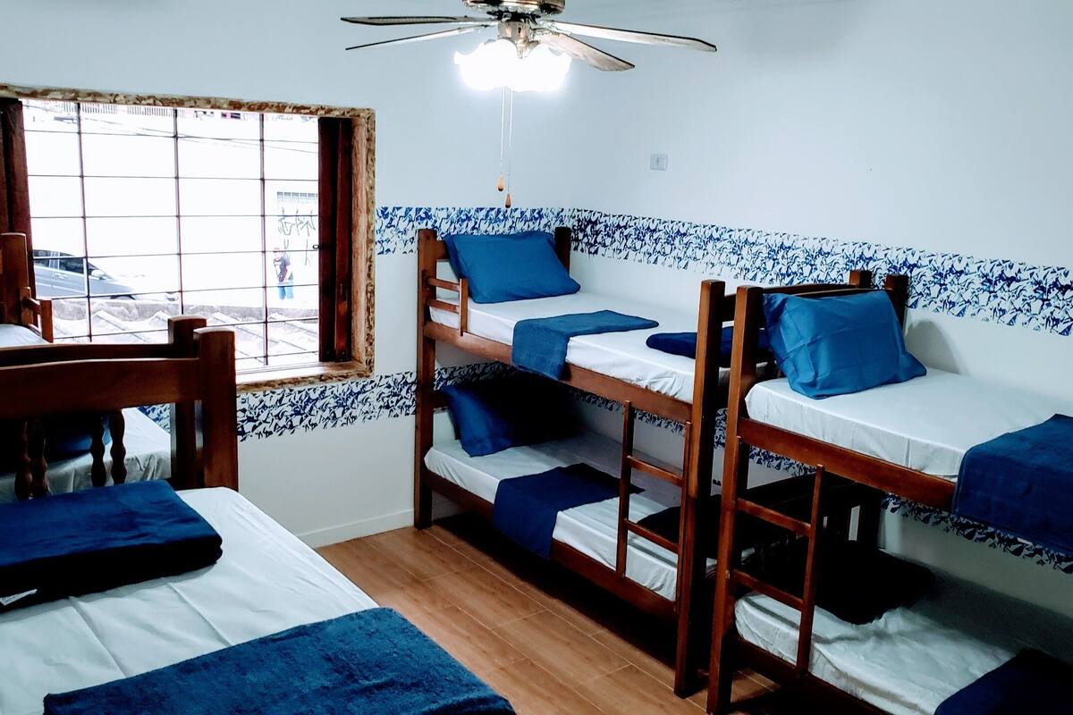 A dormitory room with bunk beds, a window, and a ceiling fan.